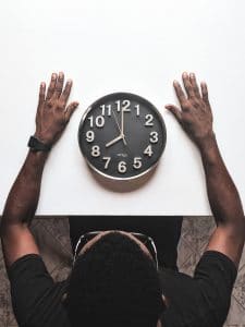 Un homme assis devant une table avec une horloge, illustrant la réflexion sur le moment propice pour effectuer un bilan de compétences.