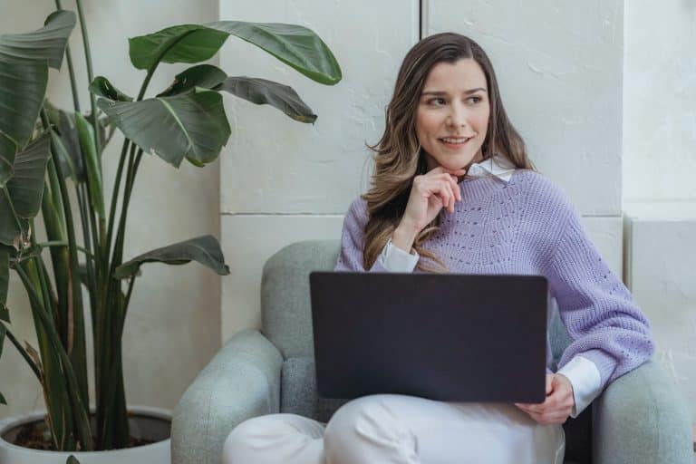 Femme souriante assise avec son ordinateur portable sur les genoux, exprimant la confiance en soi et la productivité.