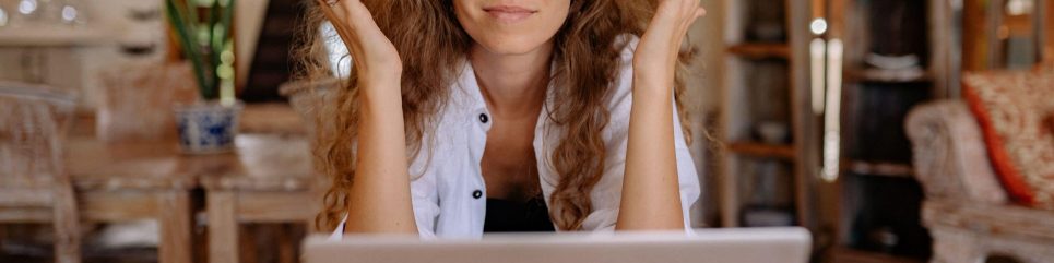 Femme devant son ordinateur, levant les deux mains en signe d'interrogation, symbole de réflexion et d'exploration pour une reconversion professionnelle.